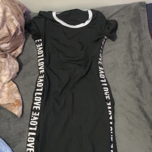 Svart ribbad kortklänning med text - Svart ribbad kortklänning med vit kant vid halsen och texten 'LOVE' längs båda sidorna. Klänningen har korta ärmar och en sportig vibe, perfekt för dig som gillar streetstyle och tydliga detaljer. Från SHEIN har inte använt den bsrs typ 4 gånger 