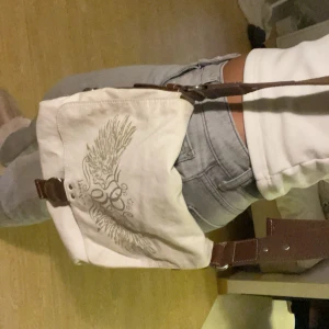 Vintage Beige axelväska från Esprit med tryck - Cool beige axelväska från Esprit med brunt justerbart band och snyggt vingmönster på locket. Väskan har detaljer i brunt konstläder och praktiska innerfack med dragkedja. Perfekt för dig som vill ha en unik och rymlig väska med streetkänsla. Nackdel - smutsig men går säkert att tvätta bort har ej testat💫