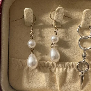 Hängande örhängen med pärlor - Säljer ett par eleganta hängande örhängen med vita pärlor i både rund och droppform. Örhängena har guldfärgade krokar och ger en klassisk vibe💛