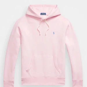 Ljusrosa hoodie från Polo Ralph Lauren/äkta från Johells - Säljer en ljusrosa hoodie från Polo Ralph Lauren med klassisk huva och snörning. Tröjan har en broderad logga i ljusblått på bröstet och en stor känguruficka framtill. Perfekt för dig som gillar stilren och bekväm streetwear.