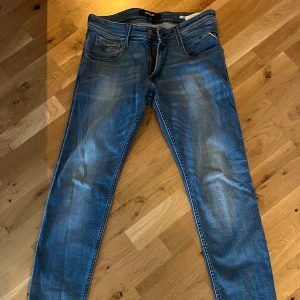 Blå Replay Anbass jeans, storlek 30 - Säljer ett par snygga Replay Anbass jeans i klassisk blå tvätt. Jeansen har fem fickor, dragkedjegylf och diskreta slitningar. Modellen är slim och passar perfekt till en avslappnad stil. Märke och storlek syns tydligt på insidan. Köptes i somras. Storlek 30:32