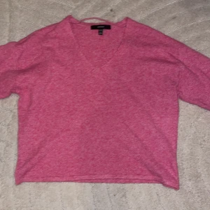 Rosa stickad tröja från Vero Moda - Mysig rosa stickad tröja från Vero Moda med v-ringad hals och långa ärmar. Perfekt för lager-på-lager och chill dagar. Ribbstickade muddar vid ärmslut och nederkant ger en snygg detalj. Enkel att matcha med jeans eller kjol.