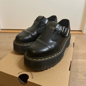 Dr. Martens svarta platå Mary Janes - Säljer ett par svarta Dr. Martens Mary Jane-skor i skinn med chunky platåsula och klassisk gul söm. Skorna har rund tå, spänne i silver och  platt sula. Tyvärr är sulorna trasiga som man kan se på bilderna.