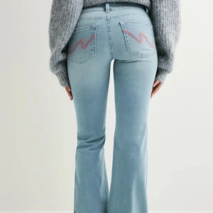 Ljusblå bootcut jeans med broderi - Snygga ljusblå jeans med bootcut-modell och hög midja. Jeansen har två knappar framtill och coola röda broderade detaljer på bakfickorna. Tillverkade i stretchig denim som sitter skönt och formar sig efter kroppen.‼️ De är uppsydda så att de passar mig som är 160cm ‼️