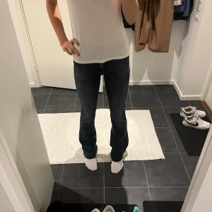 Mörkblå bootcut jeans - Snygga mörkblå jeans med bootcut passform och klassisk femficksdesign. Jeansen är mid waist och är tillverkade i ett stretchigt denimtyg som sitter skönt och formar sig efter kroppen. Perfekta för dig som gillar en tidlös och trendig look.