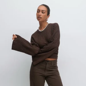 Brun topp med vida ärmar - Säljer en brun croppad tröja från Bilbos med unikt vågigt mönster och extra vida långärmar. Tröjan har en rund halsringning och är gjord i ett mjukt syntetmaterial som känns skönt mot huden. Perfekt för dig som gillar trendiga och avslappnade plagg. Tröjan har fått en repa baktill men inget som inte går att fixa enkelt. 