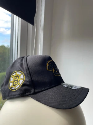 Boston Bruins keps NHL - Snygg svart keps med Boston Bruins-logga broderad framtill och på sidan. Klassisk böjd skärm och justerbar passform. Tillverkad i slitstarkt tyg och perfekt för dig som gillar sportig stil och hockey. Använd några gånger