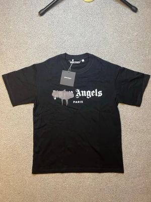 Svart Palm Angels t-shirt med tryck - Svart t-shirt från Palm Angels med klassiskt tryck framtill i vitt och grått. T-shirten har rund halsringning och korta ärmar. Perfekt för en streetwear-look och enkel att matcha med jeans eller shorts.