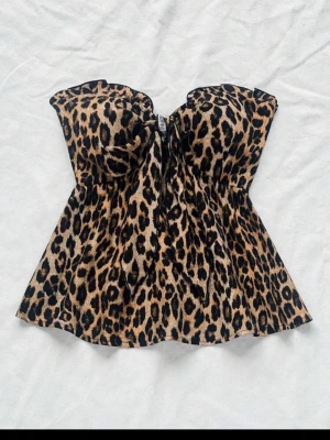Leopardmönstrad axelbandslös topp - Snygg axelbandslös topp med leopardmönster och lätt utsvängd passform. Toppen har en söt knytning framtill och volangkant upptill. Perfekt för dig som vill sticka ut med ett djurmönster.
