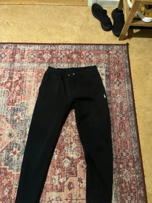 Svarta mjukisbyxor Polo Ralph Lauren - Svarta mjukisbyxor från Polo Ralph Lauren med dragsko i midjan och diskret logga på vänster ben. Tillverkade i mjukt material som passar perfekt för chill dagar. Klassisk och enkel design som funkar till det mesta.