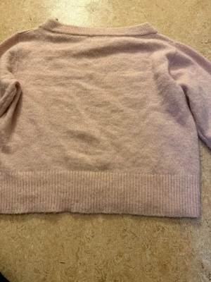 Ljusrosa stickad tröja off shoulder - Mysig ljusrosa stickad tröja med långa ärmar och bred ribbstickad kant nedtill och är Off shoulder. Tröjan har en enkel och klassisk design, perfekt för lager på lager och passar till det mesta. Materialet ser mjukt och skönt ut.