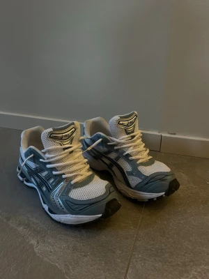 Asics gel kayano 14 - Snygga sneakers från Asics i vitt och grått med mesh- och syntetmaterial. Skorna har klassisk snörning, sportig design och tydliga Asics-loggor på sidan och tungan. Perfekta för dig som gillar en clean och trendig look.