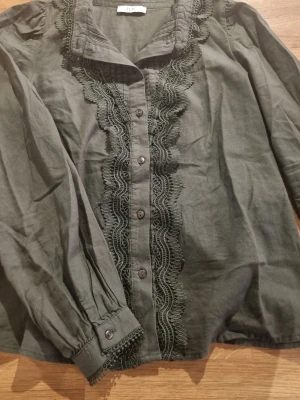 Mörkgrön blus med spetsdetaljer - Stilren mörkgrön blus från JDY med långa ärmar och dekorativa spetsdetaljer längs knäppningen framtill. Passar xs till s, #baggyjeans #lowwaist jeans #cargobyxor #vida jeans #flarejeans #lågmidja #rakajeans #kostymbyxor #mjukisbyxor #oversizedhoodie #ziphoodie #stickadtröja #corsettopp #offshoulder #babytee #linne med spets #oversized tshirt #stickadväst #maxikjol #y2k #vintage #streetwear #oldmoney #cleangirl #basic #festkläder #vardagskläder #unisex #oversized #fitted #cozy #retro #zara #hm #b