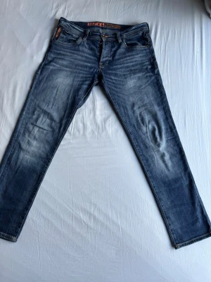 Blå slim fit jeans från Jack & Jones - Snygga blå slim fit jeans från Jack & Jones med slitningar och tvättade detaljer. Klassisk femficksmodell med orange sömmar och låg midja. Perfekta för en avslappnad och trendig stil.
