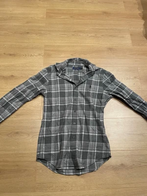 Grå rutig skjorta från Polo Ralph Lauren - Säljer en grå och vit rutig skjorta från Polo Ralph Lauren i slim fit-modell. Skjortan har långa ärmar, klassisk krage och knäppning framtill. Perfekt för dig som gillar en clean och stilren look.