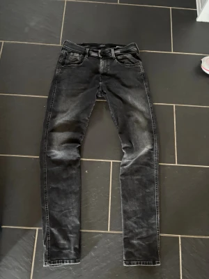Replay anbass jeans - Säljer ett par svartajeans från Replay med slitna detaljer och tvättad look. Jeansen har fem fickor, normal midja och smal passform hela vägen ner. Klassisk Replay-lapp bak i midjan och snygga sömmar. W30 L 34