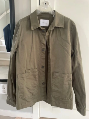 LES DEUX overshirt - Stilren olivgrön overshirt från Les Deux med klassisk krage och stora framfickor. Tillverkad i ett mjukt bomullstyg och stängs med knappar framtill. Perfekt lager-på-lager-plagg för en avslappnad look. Pris diskuterbalt hör av dig!