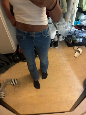 Blå bootcut jeans med låg midja - Säljer ett par blå bootcut jeans med låg midja och klassiska fem fickor. Jeansen har en snygg passform som sitter tajt upptill och släpper ut vid benen. Perfekta till en enkel topp eller hoodie för en chill look.