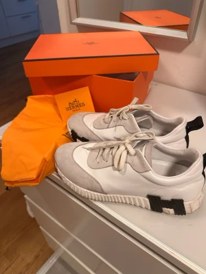 Vita och gråa sneakers  - Snygga sneakers i vitt och ljusgrått med detaljer i mocka och läder. Skorna har vita snören, svart detalj på hälen och en chunky sula med räfflat mönster. Kommer med kartong och dustbag.
