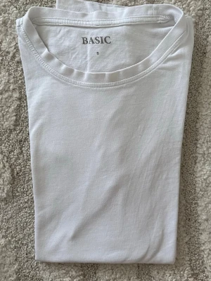 Vit basic t-shirt i bomull - En klassisk vit basic t-shirt i mjuk bomull. T-shirten har rund halsringning och korta ärmar, perfekt att matcha med allt. Enkel och stilren design utan tryck eller detaljer.