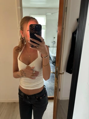 Vit halterneck topp med broschdetalj - Säljer en vit halterneck topp med en snygg broschdetalj framtill. Toppen är croppad och har en åtsittande passform som framhäver figuren. Perfekt för dig som vill ha en trendig och stilren look i sommar.