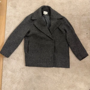 Grå ullkappa från H&M - Stilren grå kappa från H&M i ullmix med bred krage och rak passform. 