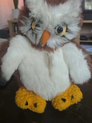 Mjuk uggla i plysch, ca 30 cm - Söt uggla i mjuk plysch med vita och bruna fjädrar, orange näbb och stora gula fötter. Ugglan har detaljer runt ögonen och är cirka 30 cm hög. Perfekt som prydnad eller gosedjur.