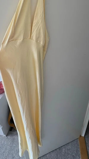 Ljusgul långklänning i satin  - Säljer en elegant ljusgul långklänning i satin med djup v-ringning och smala axelband. Klänningen har en mjuk, glansig yta och en figurnära passform. Från märket Amisu storlek 42 (passar M/L) endast testat och dragkedjan kan vara svår samt sminkfläck som går bort enkelt i tvätten💛