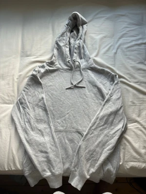 Ljusgrå hoodie från 157 - En stilren ljusgrå hoodie från 157 med klassisk huva och dragsko. Hoodien har en stor magficka och ribbade muddar vid ärmslut och nederkant. Perfekt för en avslappnad och bekväm look. Tillverkad i mjukt sweatshirtmaterial.         (Använd en gång)