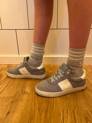 Ljusblåa-vita sneakers med mockadetaljer - Snygga sneakers i blått och vitt med klassisk låg profil. Skorna har mockaliknande material på ovandelen och vita detaljer på sidan, häl och snörning. Perfekta för en avslappnad och trendig stil. Passar till jeans eller shorts.