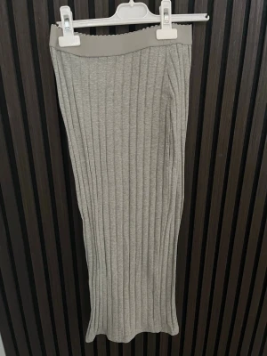 Ljusgrå ribbad långkjol - Säljer en ljusgrå långkjol med ribbad struktur. Kjolen har en rak passform och är tillverkad i ett mjukt, stretchigt material som ger en bekväm känsla. Perfekt att styla med en enkel topp eller hoodie.