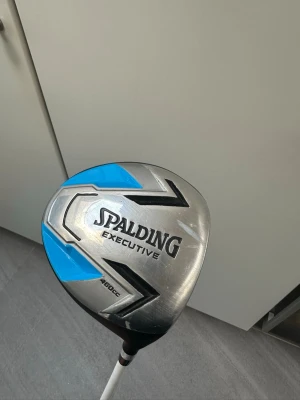 Spalding Executive golfklubba - Golfklubba Spalding Executive 460cc med silverfärgat klubbhuvud och blåa samt svarta detaljer. Medföljer svart och blått headcover med vit kant och siffran 1. Perfekt för dig som vill ha en snygg och funktionell driver till golfbanan.