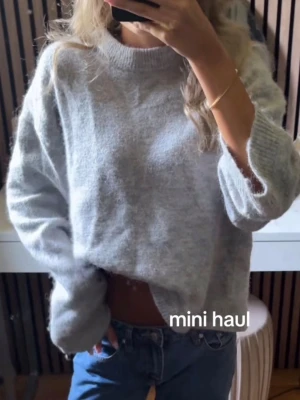 Ljusgrå oversized stickad tröja - Mysig ljusgrå stickad tröja med oversized passform och rund hals. Tröjan har långa ärmar och är tillverkad i ett fluffigt, mjukt material som ger en avslappnad look. Perfekt att styla med jeans för en chill vibe.
