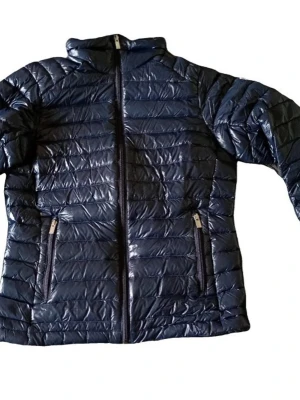 Peak Performance Pufferjacka - dam - Snygg mörkblå pufferjacka med glansig finish och horisontella sömmar. Jackan har hög krage, dragkedja framtill och två fickor med dragkedja.
