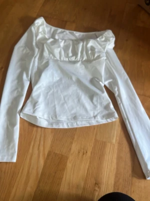 Vit långärmad topp från SHEIN - Säljer en vit långärmad topp från SHEIN i storlek XS. Toppen har en söt rynkad detalj vid bysten och en lätt figurnära passform. Perfekt att styla med jeans eller kjol för en trendig look.