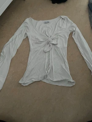 Vit långärmad topp med knyt - Säljer en vit långärmad topp med snygg knytning framtill. Toppen har en mjuk och lätt känsla, perfekt för dig som gillar en enkel men trendig stil. Passar till både jeans och kjol för en chill look.