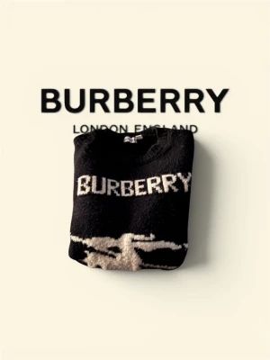 Svart stickad tröja från Burberry - Snygg svart stickad tröja från Burberry med vit logga och motiv av riddare på häst framtill. Tröjan har rund halsringning och långa ärmar. Perfekt för dig som vill ha en statement piece i garderoben.