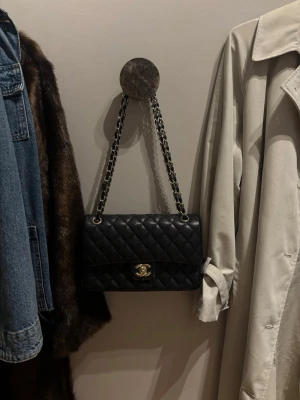 Svart quiltad handväska - Snygg svart handväska i quiltat läder med kedjerem i silver och läderdetaljer. Klassisk rektangulär form och vridlås framtill i metall. Perfekt accessoar för att lyfta vilken outfit som helst. Kan tyvärr inte garantera 100% äkthet då den är köpt begagnad.