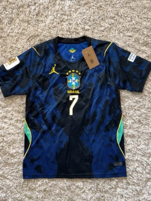 Brasilien Vini Jr. matchtröja blå - Snygg blå och svart matchtröja för Brasilien med nummer 7 och VINI JR. på ryggen. Tröjan har gula detaljer, CBF-logga på bröstet och är tillverkad i ett lätt, ventilerande material perfekt för fotboll. Korta ärmar och sportig passform.