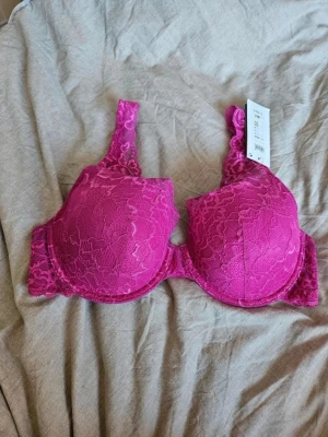Rosa spets-bh med vaddering - Snygg bh i stark rosa färg med vadderade kupor och bygel. Bh:n är täckt av blommig spets och har breda, spetsiga axelband för extra stöd och en feminin look. Perfekt för dig som vill ha något både bekvämt och stilrent.