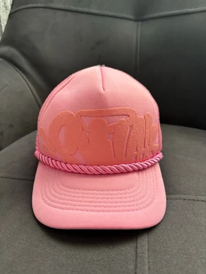 Rosa syna world cap - Snygg rosa keps med broderad logga framtill och dekorativt snöre ovanför skärmen. Kepsen har mesh på insidan för extra ventilation och justerbar passform. Perfekt accessoar för en trendig streetstyle-look.