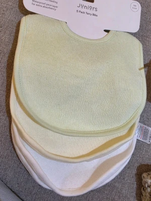 Haklapp bibs dregglis 5-pack frottéhaklappar - Säljer ett 5-pack mjuka frottéhaklappar från Juniors i ljusa pastellfärger, främst vitt och ljusgult. Haklapparna har rundad form och är perfekta för småbarn. Materialet är absorberande och har ett vattentätt lager för extra skydd. Helt nytt med tag