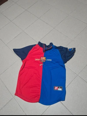 Barça jubileumströja Nike  - Säljer en FC Barcelona jubileumströja från Nike i storlek L. Tröjan är röd och blå med klubbens emblem och texten 1899-1999 på bröstet. Korta ärmar och klassisk halvkrage. Tillverkad i polyester, perfekt för fotboll eller träning. Size L but fits oversized M