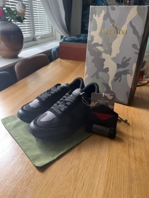 Svarta sneakers från Valentino - Stilrena svarta sneakers från Valentino Garavani med detaljer i mocka och textil. Skorna har en låg siluett och klassisk snörning. Kommer med originalkartong och dustbag. Perfekta för dig som gillar exklusiv och modern streetstyle.