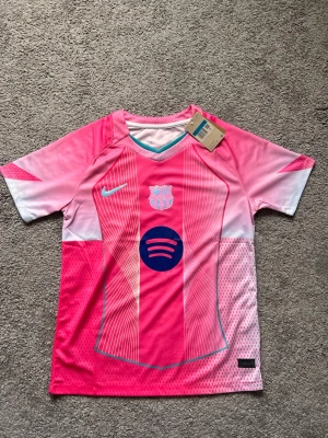 Limited Edition Rosa FC Barcelona matchtröja Nike - Säljer en rosa FC Barcelona matchtröja från Nike med vita och blå detaljer. Tröjan har klubbmärke och Nike-logga på bröstet samt Spotify-logga i mitten. Tillverkad i lätt och ventilerande funktionsmaterial, perfekt för träning eller match.