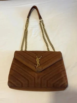 Brun mocka handväska från YSL - Snygg brun handväska i mocka från YSL. OBS väskan är välanvänd och defekter förekommer. Äkthetsbevis finns ej, därav priset❤️