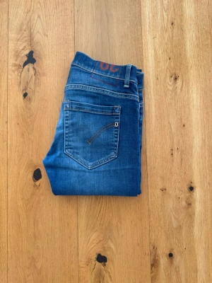 Blå jeans dondup - Snygga blå jeans i klassisk modell med raka ben och femficksdesign. Jeansen har kontrastsömmar och bälteshällor. Materialet är denim i bomull med lite stretch för extra komfort. Passar perfekt till en avslappnad stil.