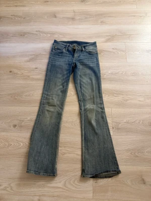 Blå bootcut jeans med slitningar - Snygga blå bootcut jeans med lätt slitna detaljer på framsidan och klassisk femficksdesign. Jeansen har låg midja och vida ben, perfekta för en avslappnad och trendig look. Tillverkade i denim med kontrastsömmar.