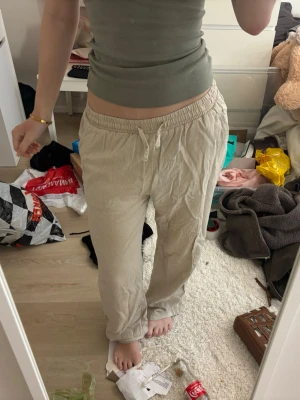 Beiga linnebyxor med dragsko - Säljer ett par beiga linnebyxor med avslappnad passform och elastisk midja med dragsko. Byxorna har raka ben och är tillverkade i ett lätt och luftigt linnematerial, perfekta för en chill och stilren look.