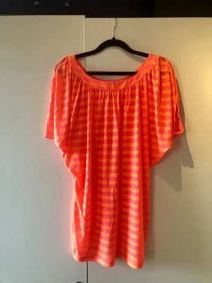 Bik Bok Randig Tröja / Topp Neonrosa & Orange – Stl XS - Härligt färgglad och luftig tröja från Bik Bok i randigt utförande med klara nyanser av neonrosa och orange. Tillverkad i en väldigt mjuk och skön viskosblandning med fint fall. Modellen har vid urringning både fram och bak, avslappnad passform och sköna batwing-ärmar. Märke: Bik Bok Storlek: XS Mått: Axelbredd ca 35 cm, längd från axeln ca 73 cm Material: 50% Viskos, 50% Polyester Skick: Mycket gott skick
